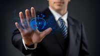 Professional businessman in dark suit displaying glowing blue digital technology interface with futuristic icons floating above palm against black background.