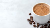 Fresh hot cocoa drink in white ceramic cup with scattered roasted coffee beans on light gray concrete background with copy space for menu design.