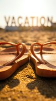 Flip flops resting on warm sandy beach with vacation sign glowing in golden sunlight, evoking summer travel and relaxation vibes.