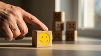 Hand selecting wooden block with yellow smiley face from row of cubes representing positive choice, customer satisfaction and feedback concept.
