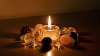 Glowing candle surrounded by healing crystals and gemstones creating peaceful meditation atmosphere for wellness and spiritual practices.