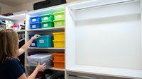 Woman organizing colorful storage bins on white shelves in closet for home organization and decluttering solutions.
