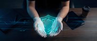 Male hands holding glowing digital shield symbol on wooden desk, representing cybersecurity protection, data safety, and network defense technology for business applications.