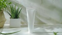 Blank white cosmetic tube on marble surface with aloe vera plant and natural decor. Clean minimalist skincare product mockup with soft shadows.