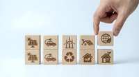 Hand selecting wooden cube with global network icon from eco-friendly energy symbols including solar panels, electric car, wind turbines and recycling.