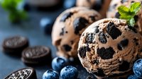 Freshly baked chocolate chip cookies with blueberries and sandwich cookies on slate surface, perfect for food photography, baking blogs, and dessert marketing materials.