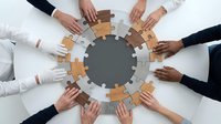 Team of diverse professionals assembling wooden puzzle pieces in circle formation, representing unity, collaboration, and business teamwork solutions for corporate training and organizational development.