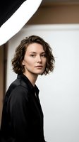 Professional young Caucasian woman with curly brown hair wearing black shirt in modern office interior with natural lighting for business portraits.