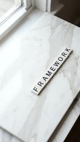 Framework word spelled out in wooden letter tiles on white marble surface near window for business planning and organizational concepts.