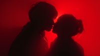 Romantic silhouette of couple in intimate moment against vibrant red background. Man and woman facing each other in tender embrace for love and relationship concepts.
