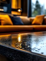 Raindrops on dark surface with warm ambient lighting create cozy atmosphere, blurred sofa with yellow and navy pillows in background, selective focus on water drops.