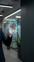 Businessperson in dark suit touching holographic display showing hand with green leaves and water droplets in modern office environment with fluorescent lighting.
