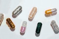 Colorful glitter-filled capsule pills scattered on white background, sparkling supplement concept for health, beauty, and wellness campaigns.