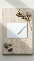 White envelope on natural travertine stone surface with olive branch and smooth pebbles for elegant correspondence and wedding stationery design.