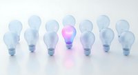 Row of light bulbs with one glowing pink bulb standing out among clear ones, representing creativity, innovation and unique thinking in business concepts.