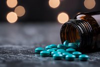 Turquoise pills spilling from brown glass bottle on dark surface with soft bokeh lights in background, dramatic medical concept for pharmaceutical industry.