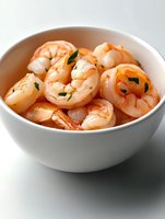 Fresh cooked shrimp garnished with herbs served in white ceramic bowl on light background, close up view of seafood appetizer for restaurant menu.