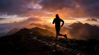 Male runner silhouette jogging on mountain ridge at dramatic sunset with golden clouds and layered peaks for fitness motivation and outdoor adventure concepts.