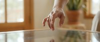 Close-up of a hand with a ring touching a glass table surface, reflection visible, warm natural light, cozy home interior background.