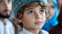 Young middle eastern boy wearing traditional turquoise cap with ornate embroidery gazes upward with innocent expression, curly hair and bright eyes against blurred background.