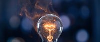 Glowing incandescent light bulb with warm filament against dark blue bokeh background, symbolizing innovation, creativity, ideas, and energy solutions for business and technology concepts.