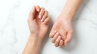 Close-up of two female Caucasian hands with natural nails on a marble surface, showcasing healthy skin and minimalist nail care.