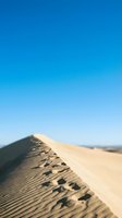 Footprints trail across a sandy desert dune ridge under clear blue sky, capturing the solitude and vastness of arid landscape exploration and travel adventure.