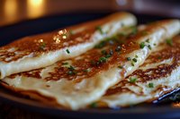 Crispy golden crepes filled with melted cheese and fresh herbs on dark plate, close-up view with selective focus showing delicate texture and garnish.