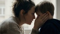 Young mother tenderly holding her toddler son's face in intimate moment of connection and love at home by window with soft natural light.