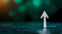 White chalk arrow pointing upward on dark textured surface with blurred teal and orange bokeh background, symbolizing growth, direction and success.