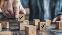 Hands arranging wooden blocks with checkmark symbols on rustic table, representing business planning, task completion and project management goals.
