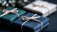 Elegant gift boxes wrapped in textured fabric with simple twine bows on dark background, creating minimalist festive composition for special occasions.