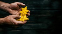 Male hands holding bright yellow star fruit against dark wooden background, suitable for food, agriculture, tropical produce, and healthy eating concepts.