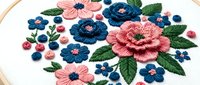 Colorful hand embroidered floral bouquet with pink and blue flowers on white fabric in wooden hoop, traditional needlework craft for home decor projects.