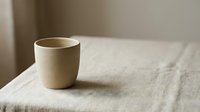 Minimalist ceramic cup on natural linen fabric with soft neutral tones and warm sunlight, suitable for home decor, lifestyle, and product photography.