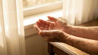 Elderly hands cupped in prayer or meditation gesture by sunny window, symbolizing hope, faith, spirituality and peaceful reflection in golden light.