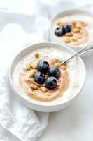 Creamy yogurt bowl with fresh blueberries, pine nuts and cinnamon swirl served in white ceramic bowl on light background, healthy breakfast concept.