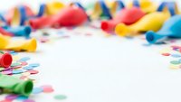 Colorful party supplies with confetti scattered around white background creating festive celebration frame for text or design elements.