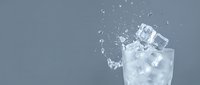 Glass of ice water with splashing cubes on gray background, suitable for beverage, refreshment, and wellness marketing materials.
