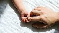 Tiny newborn hand gently holding an adult finger on a soft white fabric, symbolizing love, trust, and the bond between parent and child.