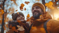 Happy Caucasian couple in warm winter clothes enjoying falling autumn leaves in park during golden hour sunset, expressing genuine joy and connection outdoors.