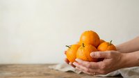 Fresh ripe oranges held in hands against neutral background, suitable for food, nutrition, healthy eating, and organic produce marketing materials.