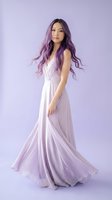 Young Asian woman with long purple hair wearing elegant lavender gown posing gracefully against matching purple background for fashion and beauty concepts.