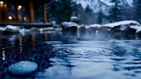 Steaming natural hot spring pool with snow covered rocks in winter twilight, rippling water surface creates mesmerizing patterns against dark blue water.