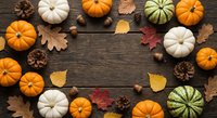 Autumn pumpkins and gourds arranged in circular frame with colorful fall leaves, pine cones and acorns on rustic wooden background for seasonal decorating.