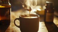 Steaming hot coffee with honey dripping from spoon into dark ceramic mug on rustic wooden table, creating cozy morning atmosphere with golden bokeh lights.