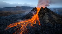 Dramatic volcanic eruption with flowing lava streams against mountainous landscape at dusk, orange magma rivers creating natural light show amid dark rocky terrain.