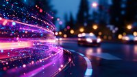 Glowing pink and purple light trails curve along dark city street with bokeh effects and defocused urban nighttime background creating magical atmosphere.