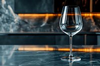 Empty wine glass on marble counter with warm lighting and blurred bar background for restaurant and hospitality industry use.