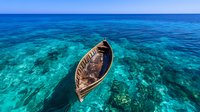 Wooden fishing boat floating on crystal clear turquoise ocean water above coral reef, aerial drone view showing tropical marine landscape and seascape.
